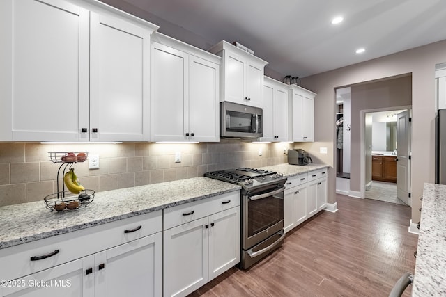 kitchen featuring white cabinetry, appliances with stainless steel finishes, decorative backsplash, and light wood-style flooring