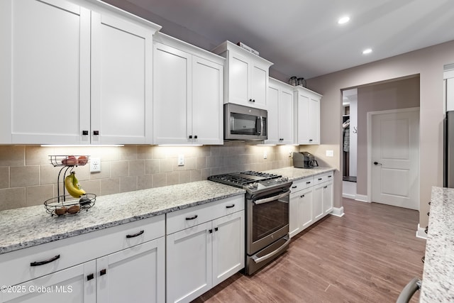 kitchen with stainless steel appliances, white cabinetry, light wood-style floors, and tasteful backsplash