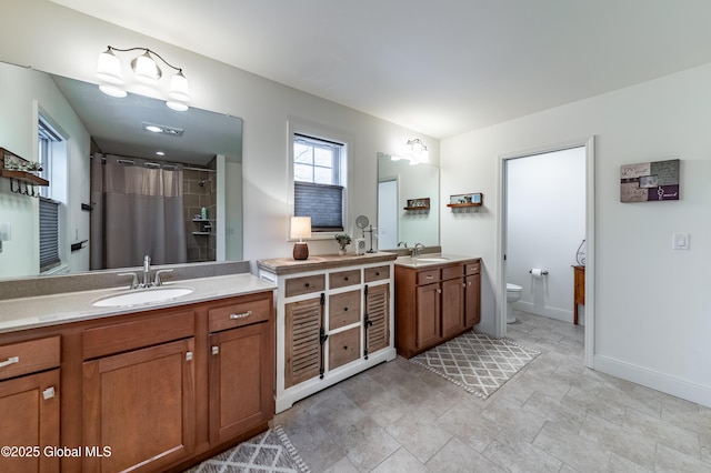 bathroom featuring two vanities, a sink, toilet, and baseboards