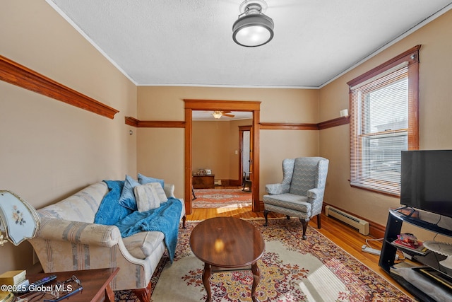 living area with a textured ceiling, ornamental molding, baseboard heating, and wood finished floors