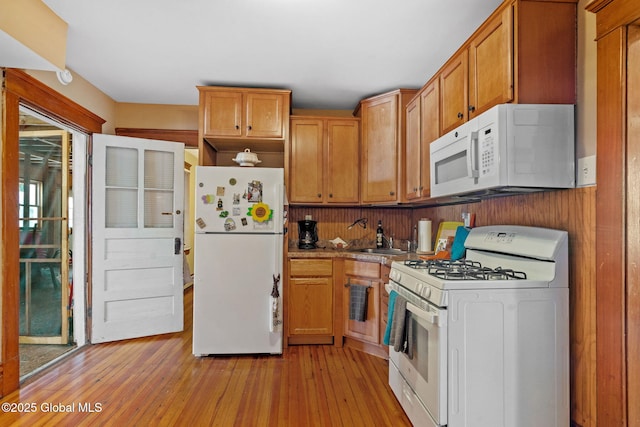 kitchen with light countertops, light wood-style floors, brown cabinetry, a sink, and white appliances