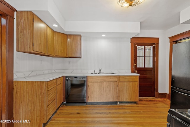 kitchen featuring brown cabinetry, light wood-type flooring, black appliances, a sink, and recessed lighting