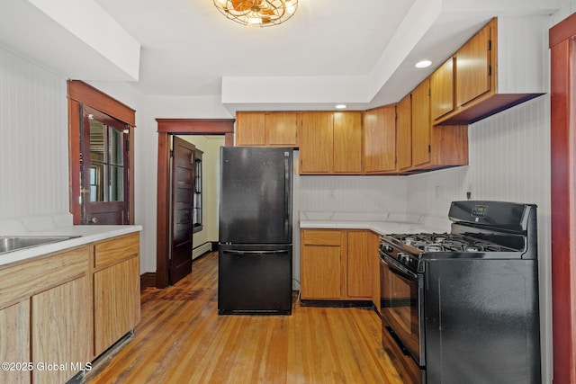 kitchen with brown cabinets, light countertops, light wood-style floors, a baseboard heating unit, and black appliances