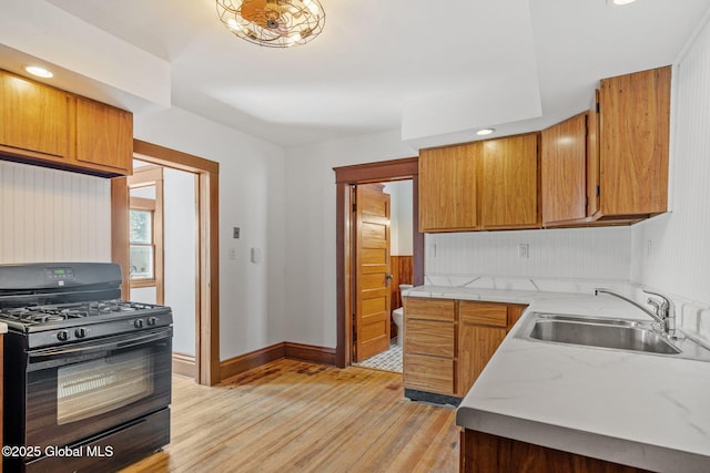 kitchen featuring brown cabinetry, black range with gas stovetop, light countertops, and a sink