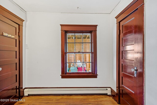 interior space featuring baseboards, baseboard heating, wood finished floors, and crown molding