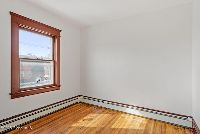 spare room featuring a baseboard heating unit and wood finished floors