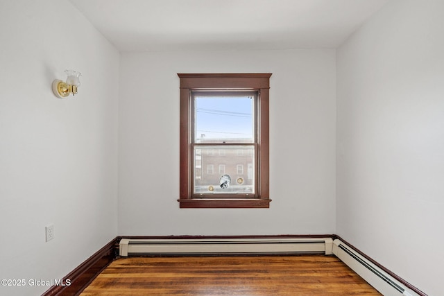 empty room featuring a baseboard radiator, baseboards, and wood finished floors