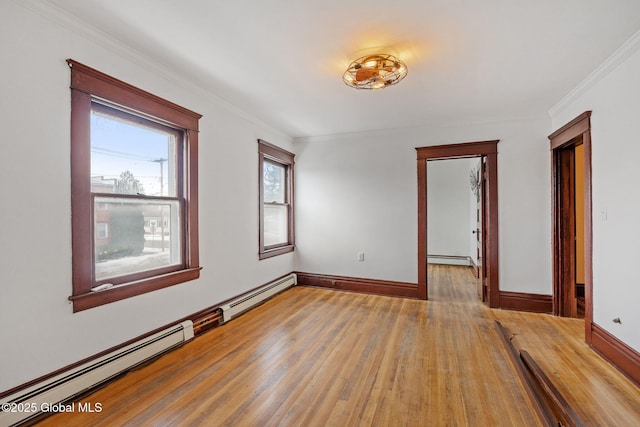 spare room featuring crown molding, light wood finished floors, baseboard heating, and baseboards