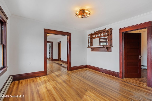 spare room featuring crown molding, baseboard heating, a baseboard heating unit, wood finished floors, and baseboards