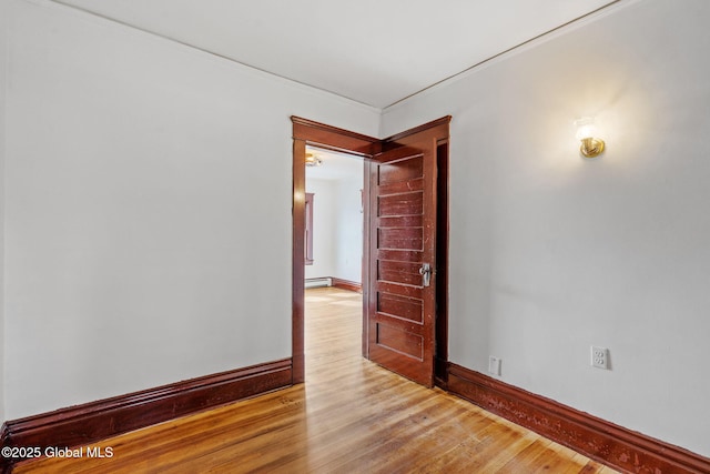 spare room featuring a baseboard radiator, baseboards, and wood finished floors