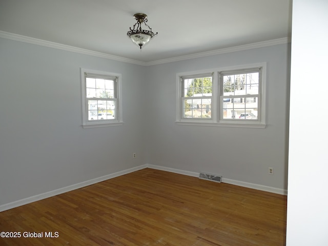 unfurnished room featuring crown molding, wood finished floors, visible vents, and baseboards