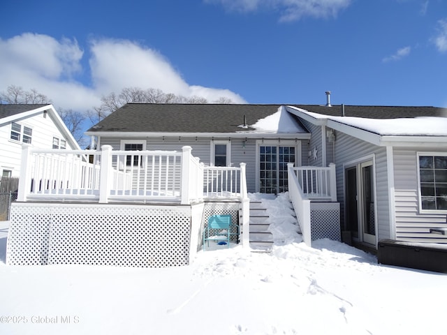 snow covered back of property featuring roof with shingles and a wooden deck