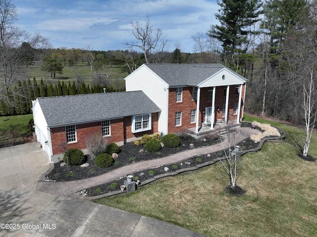 neoclassical / greek revival house with concrete driveway, a front yard, brick siding, and a shingled roof