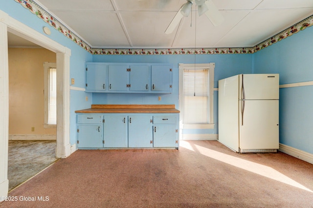 kitchen featuring blue cabinetry, butcher block countertops, light colored carpet, and freestanding refrigerator