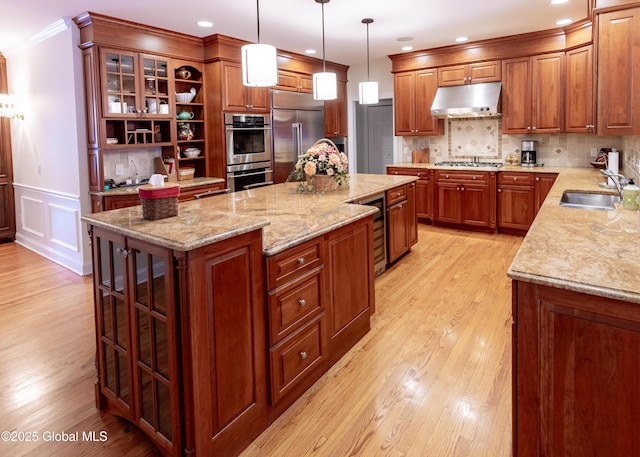 kitchen featuring appliances with stainless steel finishes, ornamental molding, a sink, a kitchen island, and under cabinet range hood