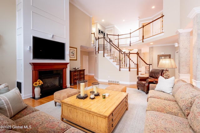 living area with a fireplace with flush hearth, visible vents, light wood-style floors, stairway, and crown molding