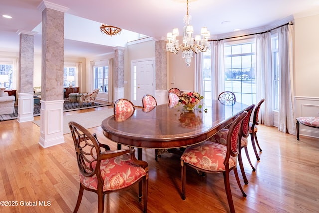 dining space featuring a wainscoted wall, decorative columns, a decorative wall, ornamental molding, and light wood-type flooring