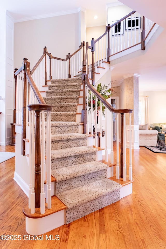 stairway featuring wood finished floors, a towering ceiling, and crown molding