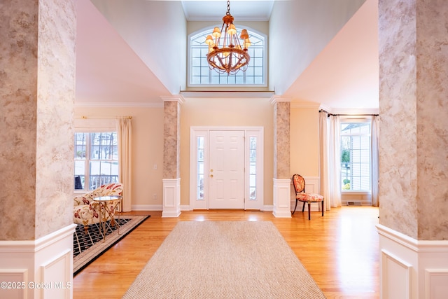 foyer entrance featuring decorative columns, ornamental molding, wood finished floors, a high ceiling, and a chandelier