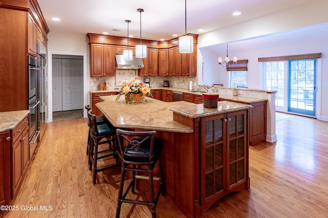 kitchen featuring decorative backsplash, appliances with stainless steel finishes, a breakfast bar area, light wood-type flooring, and under cabinet range hood