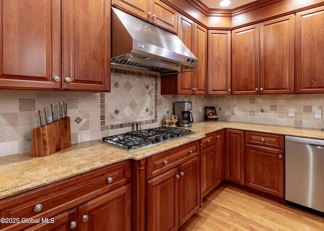 kitchen with light wood-type flooring, under cabinet range hood, appliances with stainless steel finishes, and light stone counters