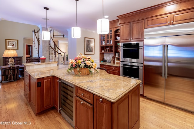 kitchen with light wood-style flooring, wine cooler, appliances with stainless steel finishes, brown cabinets, and light stone countertops