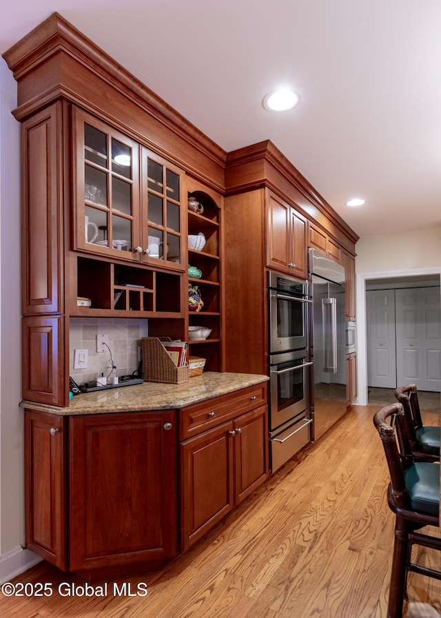 kitchen featuring light stone counters, light wood-style floors, appliances with stainless steel finishes, a warming drawer, and open shelves