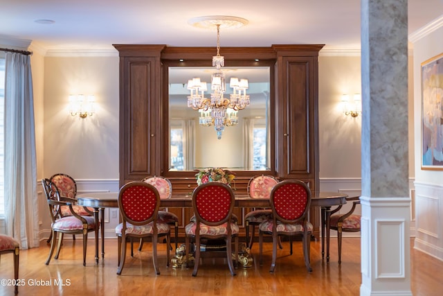 dining area with crown molding, decorative columns, an inviting chandelier, wainscoting, and wood finished floors