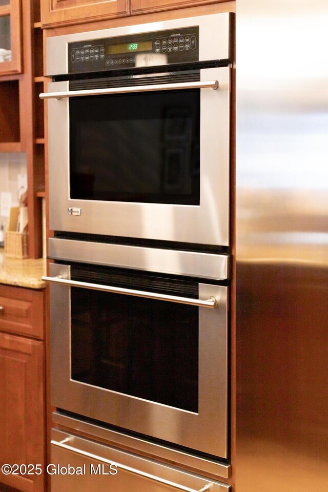 kitchen with appliances with stainless steel finishes, brown cabinets, and light stone countertops