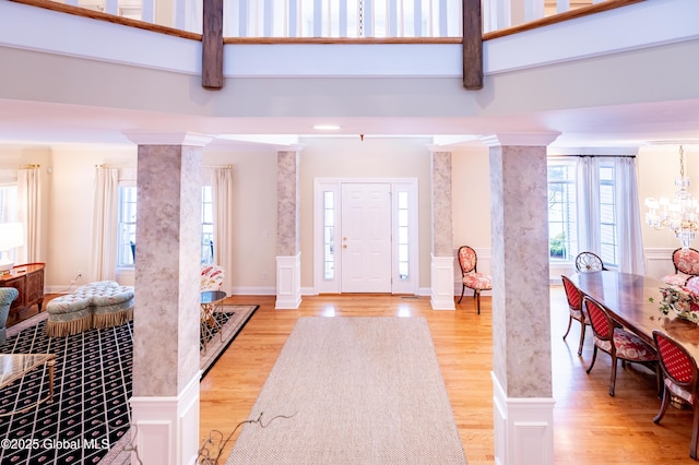 foyer with ornate columns, light wood finished floors, and a wainscoted wall