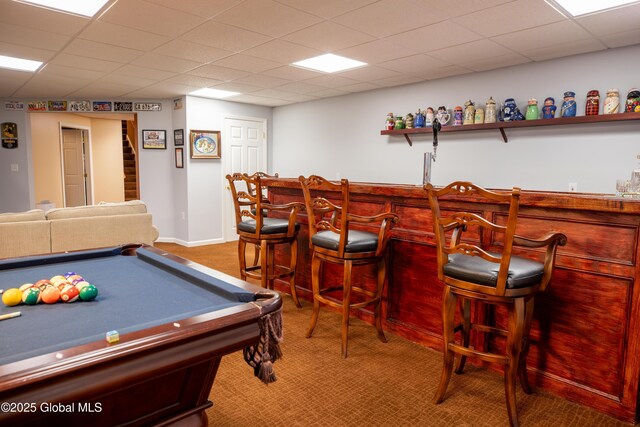 rec room featuring a paneled ceiling, baseboards, carpet flooring, and a dry bar