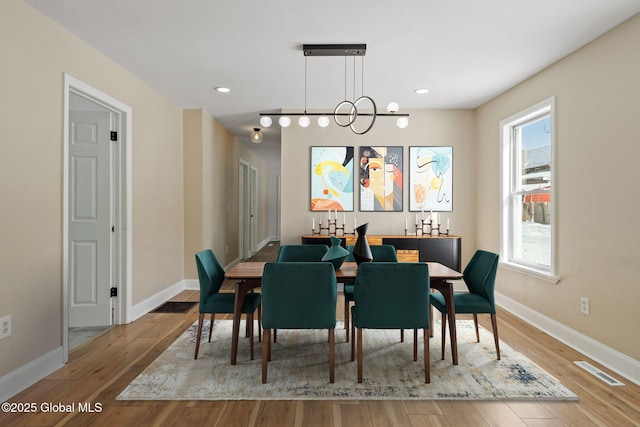 dining space with baseboards, visible vents, a chandelier, and wood finished floors