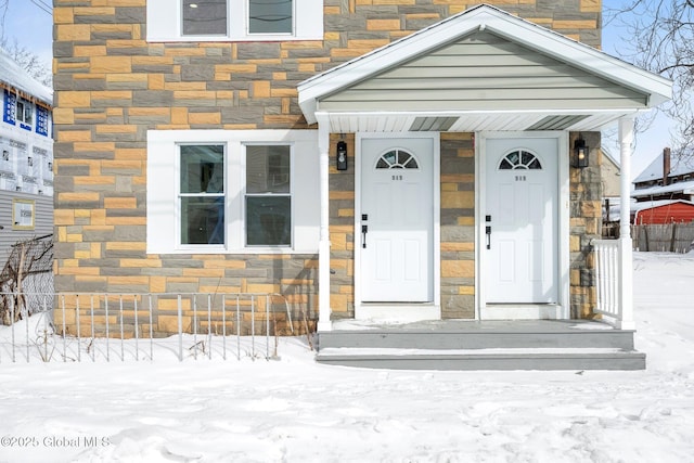 snow covered property entrance with stone siding and a chimney