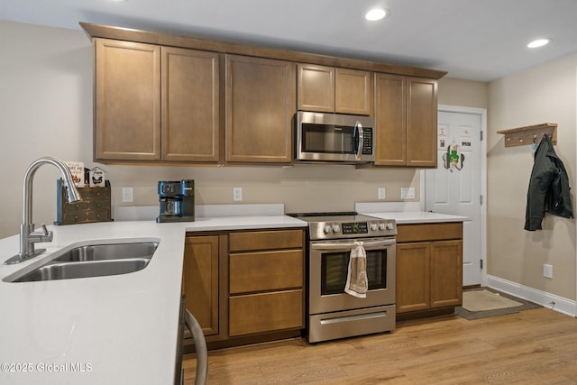 kitchen with stainless steel appliances, light wood-style floors, light countertops, and a sink