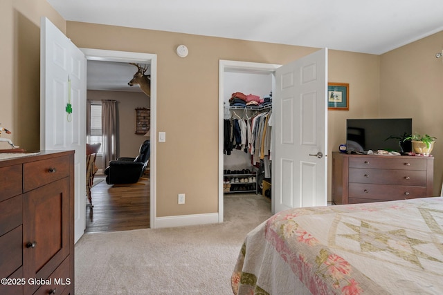 bedroom with a spacious closet, baseboards, a closet, and light colored carpet