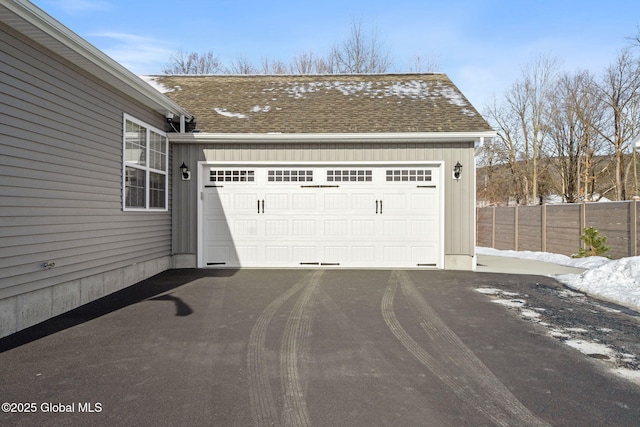 snow covered garage with aphalt driveway and fence