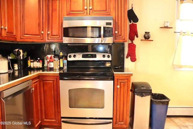 kitchen featuring light tile patterned floors, a baseboard radiator, stainless steel appliances, decorative backsplash, and dark countertops