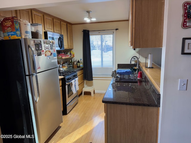 kitchen featuring light wood finished floors, dark stone counters, brown cabinetry, appliances with stainless steel finishes, and ornamental molding