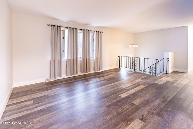 unfurnished room with an inviting chandelier, baseboards, and wood finished floors