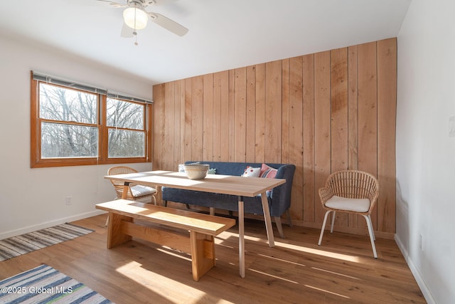 dining area featuring ceiling fan, wooden walls, baseboards, and wood finished floors