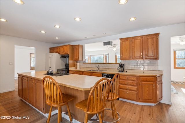 kitchen featuring decorative backsplash, a center island, freestanding refrigerator, light countertops, and a sink