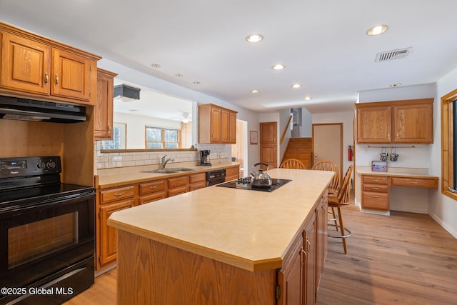 kitchen featuring built in desk, visible vents, a sink, under cabinet range hood, and black appliances