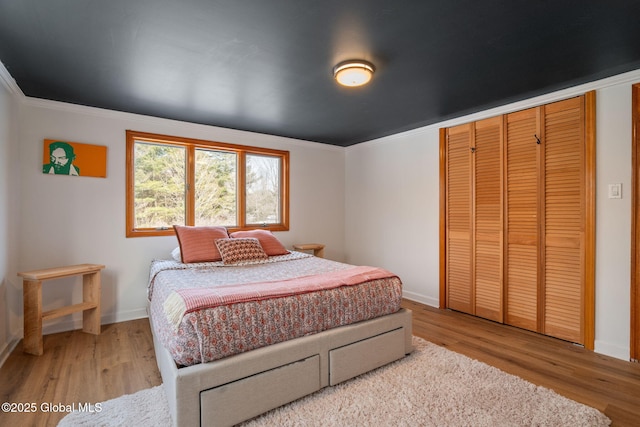 bedroom featuring light wood-type flooring, a closet, crown molding, and baseboards