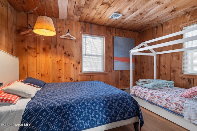 bedroom with wooden ceiling, wood finished floors, visible vents, and wooden walls