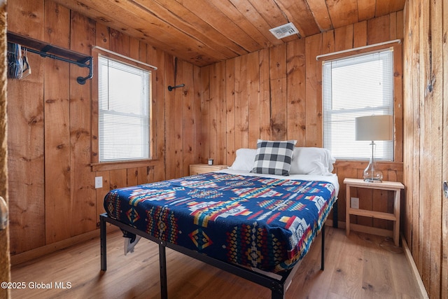 bedroom with light wood-type flooring, wooden ceiling, visible vents, and wooden walls