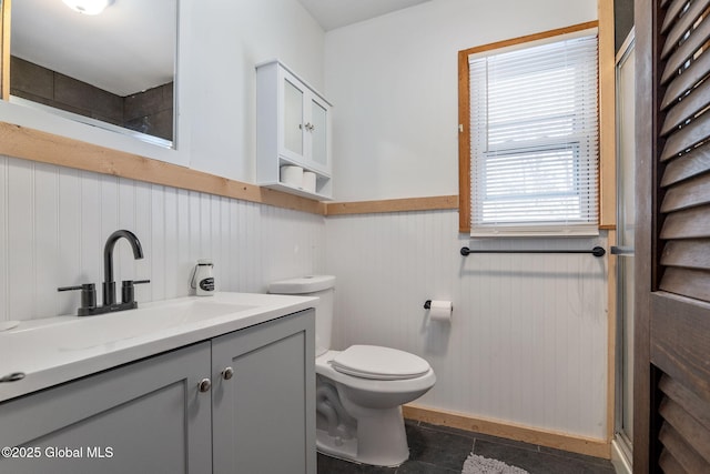 full bath with toilet, a shower with door, vanity, and wainscoting