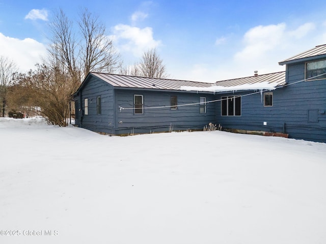 snow covered rear of property featuring metal roof and a standing seam roof