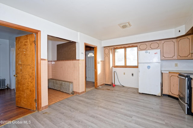 kitchen with stainless steel electric range oven, radiator, freestanding refrigerator, wainscoting, and tile walls