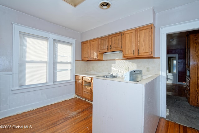 kitchen featuring visible vents, backsplash, light countertops, wood finished floors, and a sink