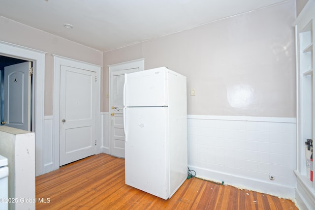 kitchen with a wainscoted wall, tile walls, wood finished floors, and freestanding refrigerator